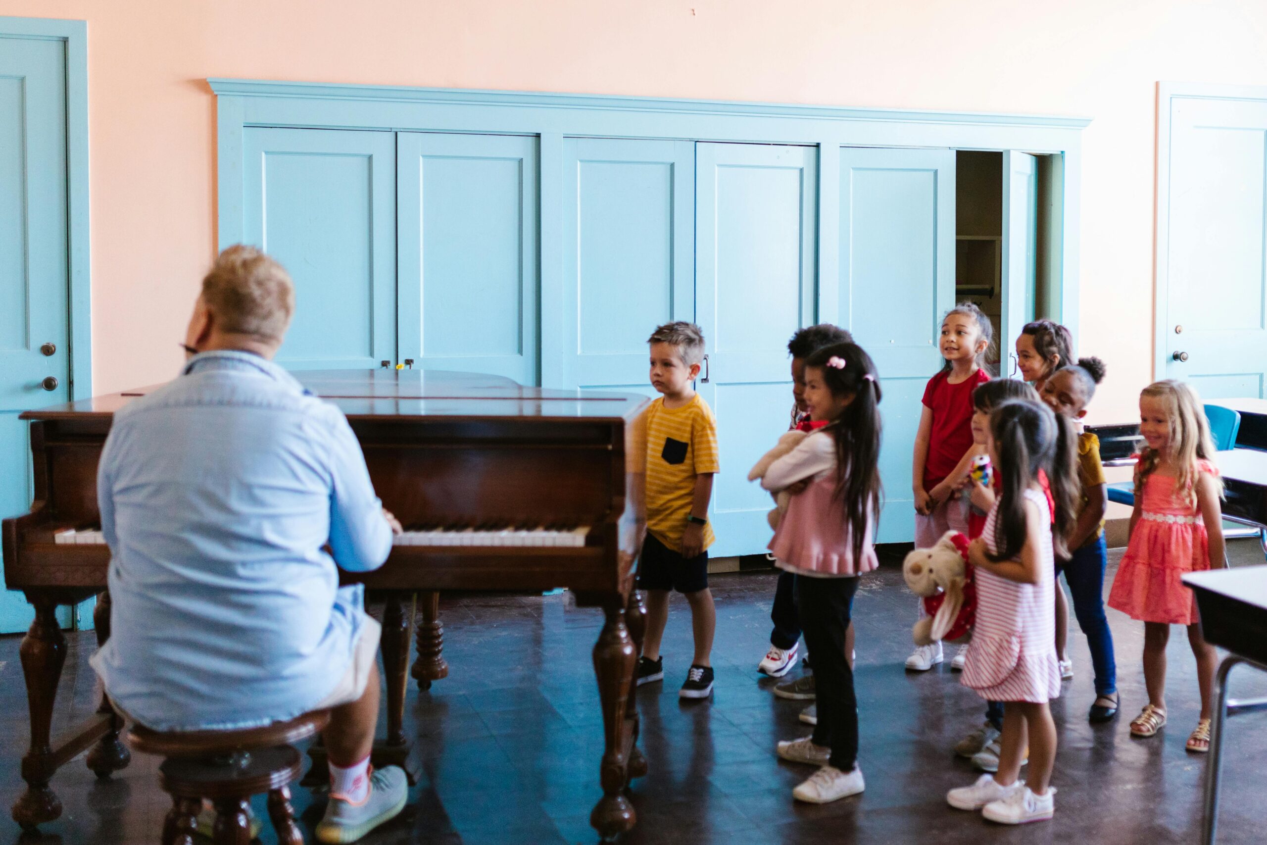 Group of children learning piano with teacher in a classroom, fostering musical education.