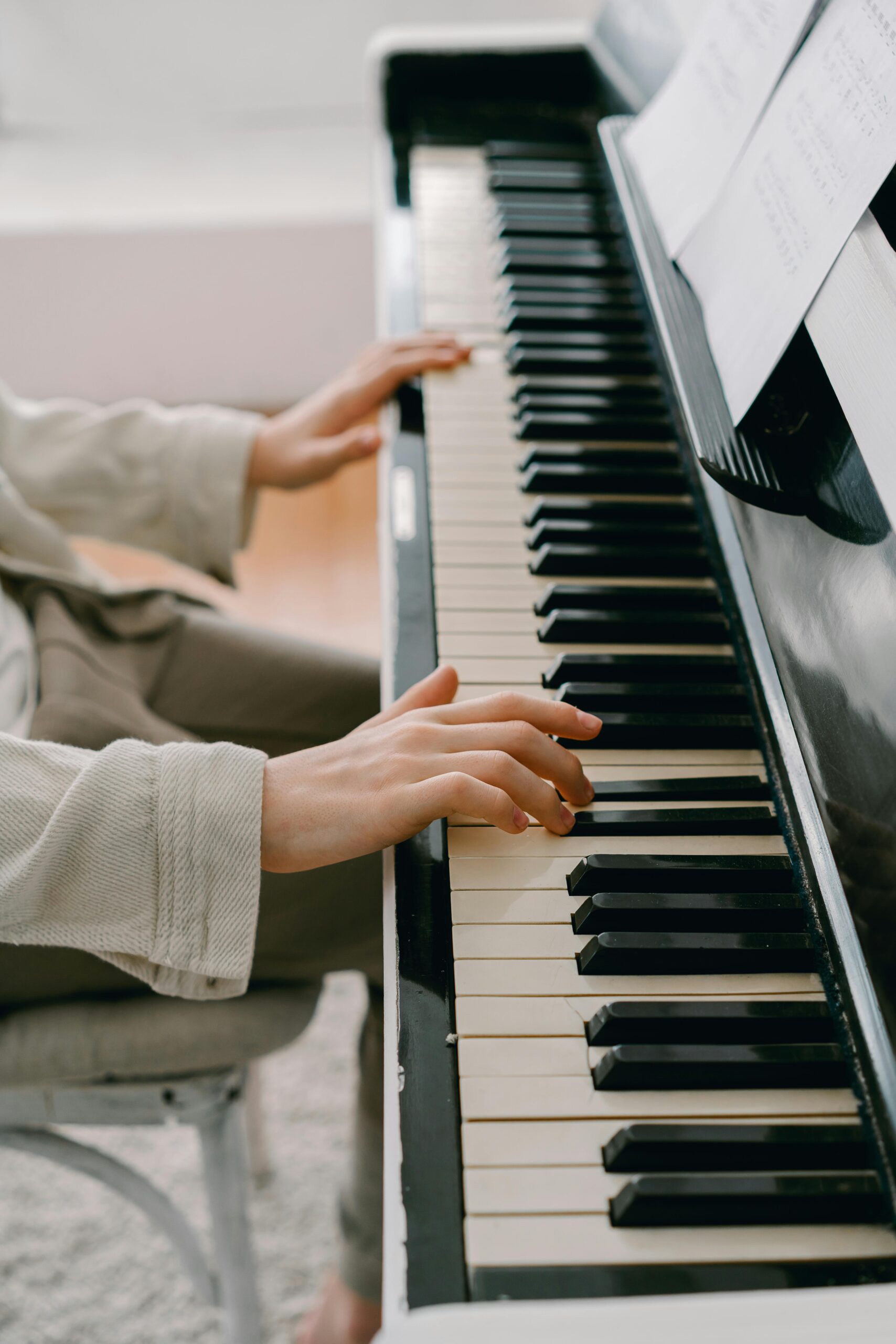 Hands playing piano with sheet music indoors, focusing on musical aesthetics.