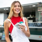 Cheerful woman in red top enjoying blue ice cream at a food truck outdoors.