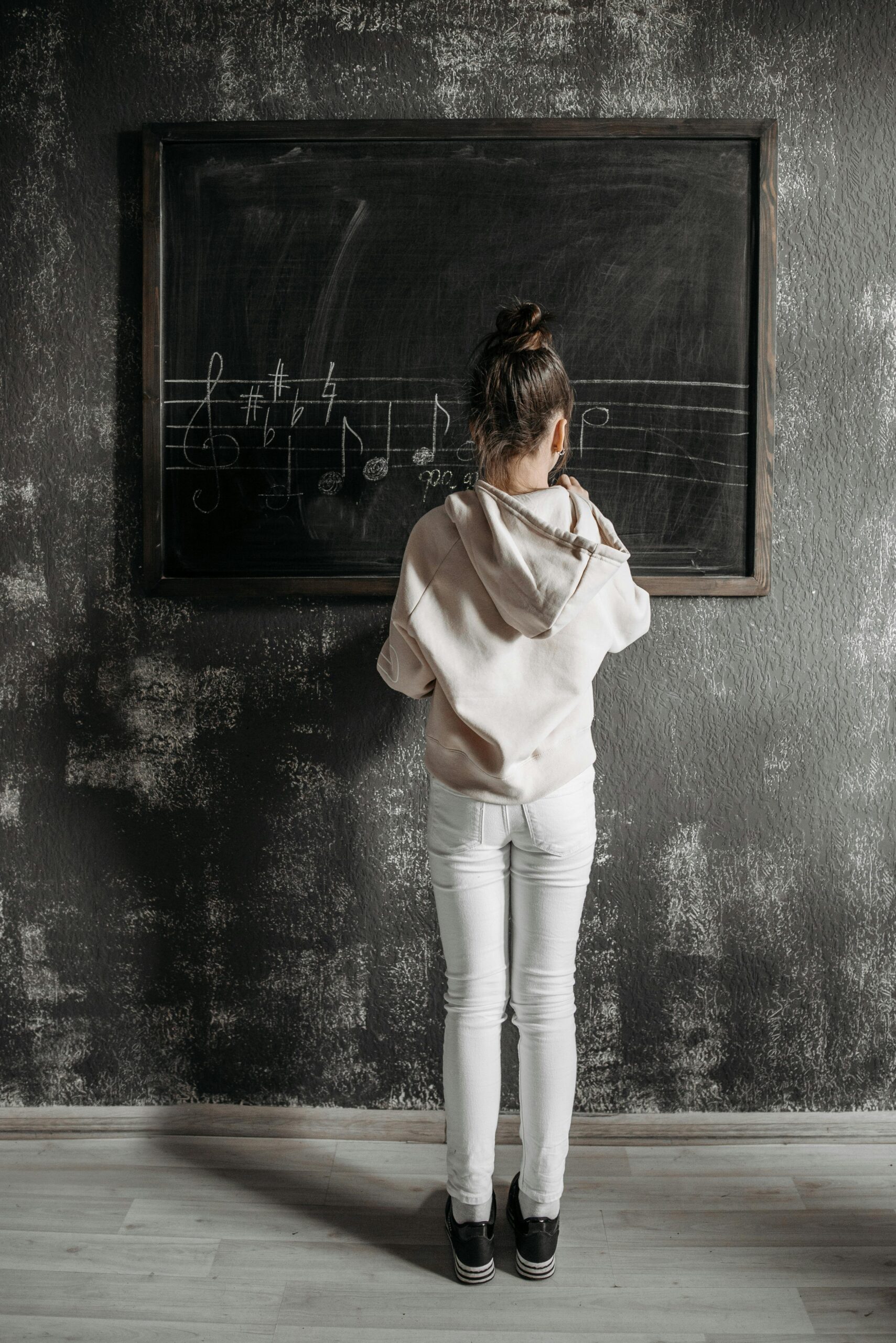 A child stands at a blackboard in a music studio writing musical notes during private lessons.