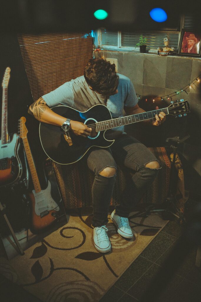 pexels-photo-2079169-2079169 A young man plays guitar in a cozy, dimly lit room, creating a musical atmosphere.