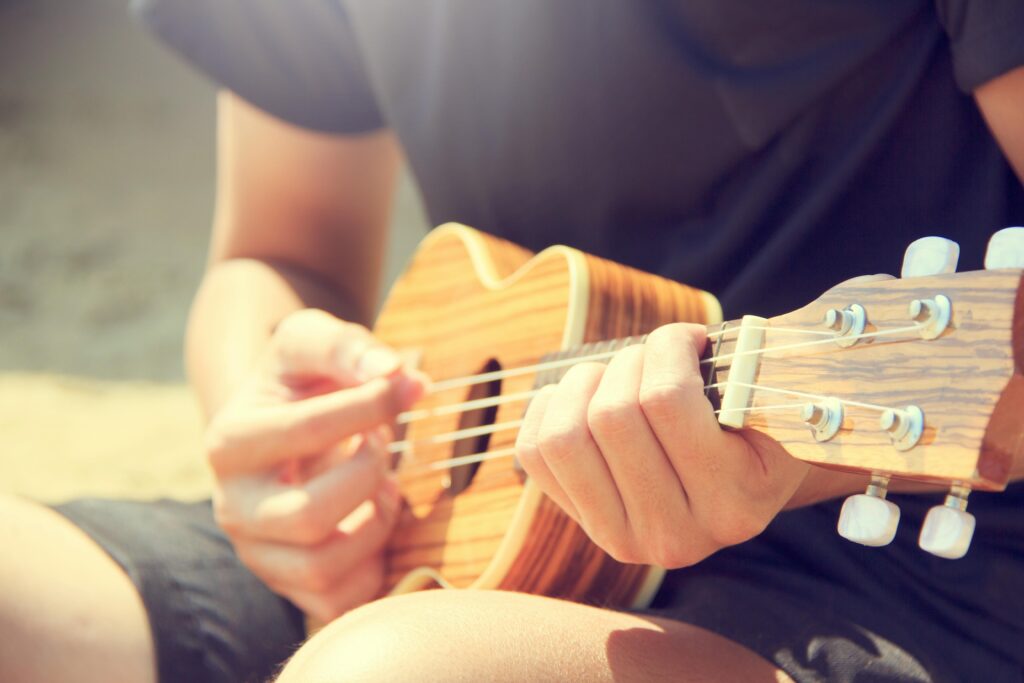 pexels-photo-346709-346709 Close-up of a man's hands strumming a ukulele outdoors on a sunny day.