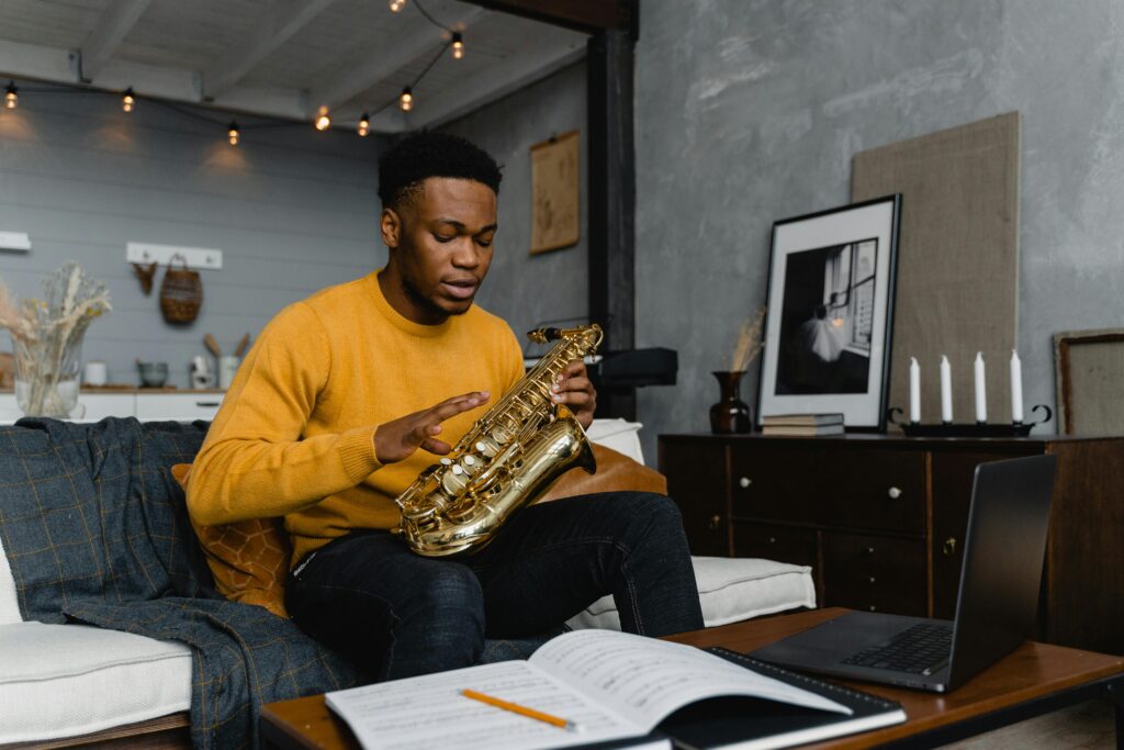 pexels-photo-6671702-6671702 Young man sitting on a couch, practicing saxophone with sheet music in a cozy living room.